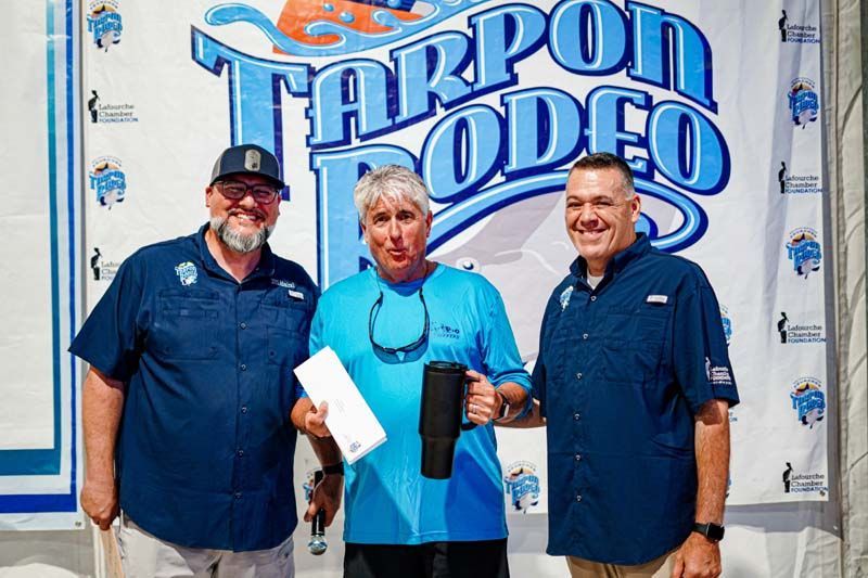 Three men are standing in front of a tarpon rodeo sign.
