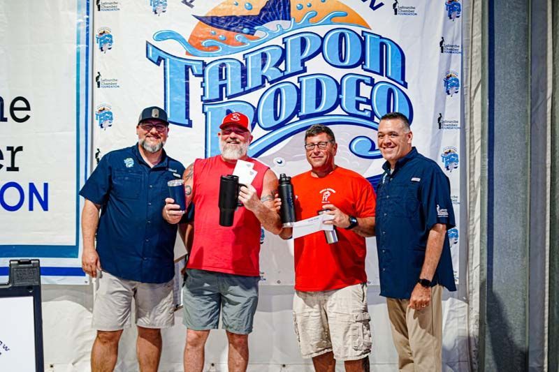 A group of men are standing in front of a tarpon rodeo sign.