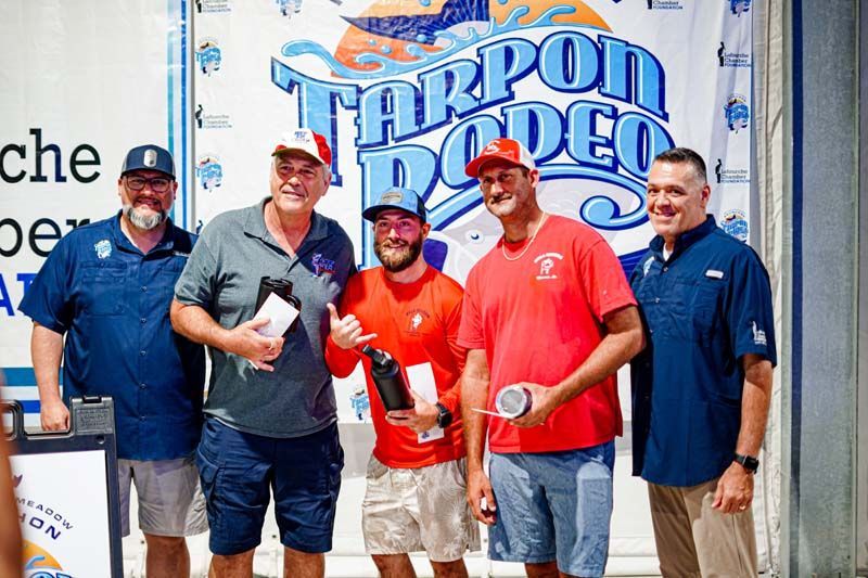 A group of men are posing for a picture in front of a tarpon rodeo sign.