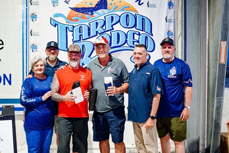 A group of people are posing for a picture in front of a tarpon rodeo sign.