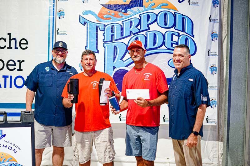 A group of men are posing for a picture in front of a tarpon rodeo sign.