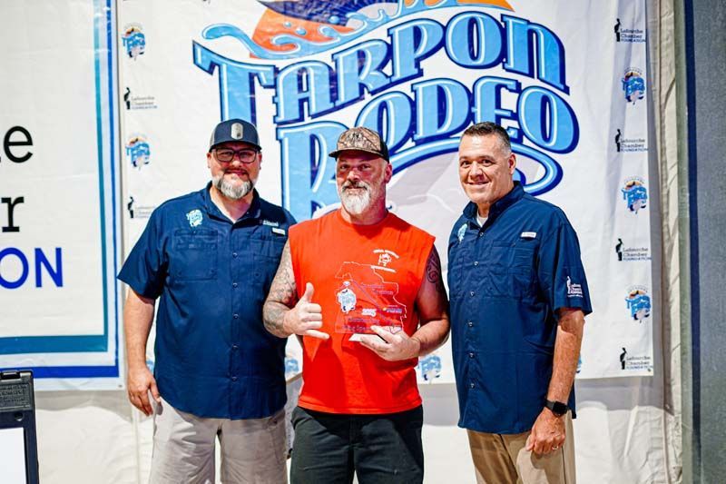 Three men are standing next to each other in front of a tarpon rodeo sign.