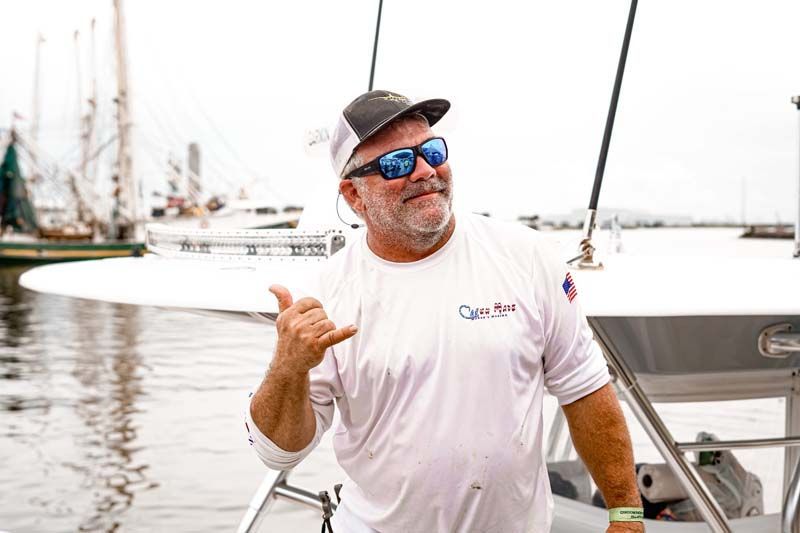 A man wearing sunglasses and a hat is standing on a boat in the water.