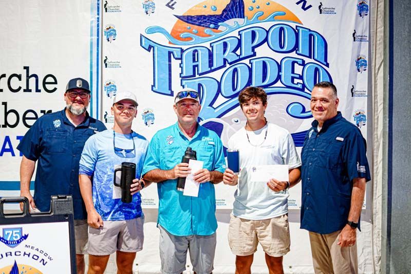 A group of men are standing in front of a tarpon rodeo sign.