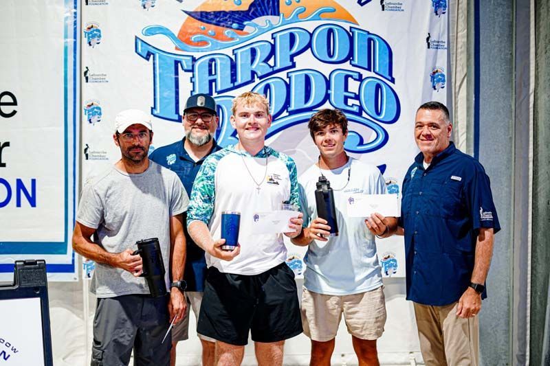 A group of men are posing for a picture in front of a tarpon rodeo banner.