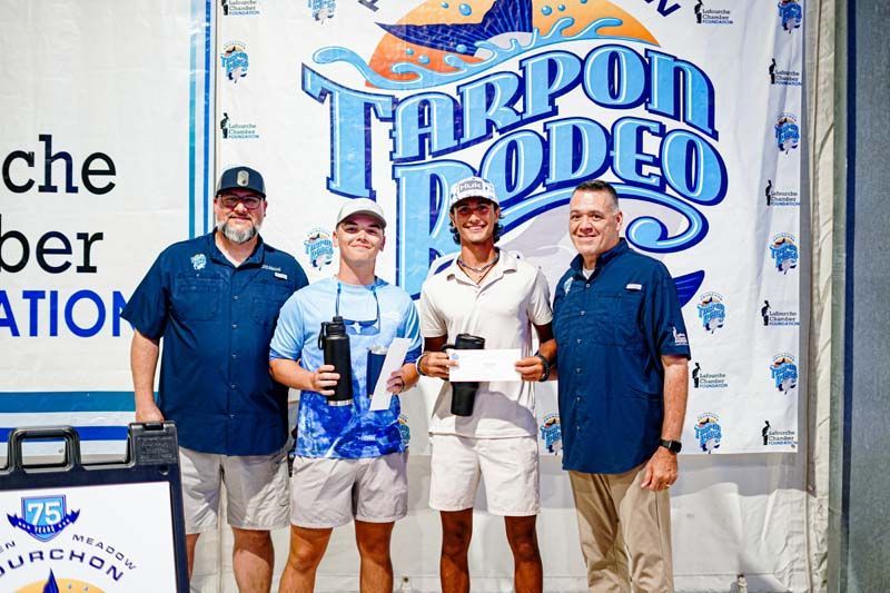 A group of men are standing in front of a tarpon rodeo sign.