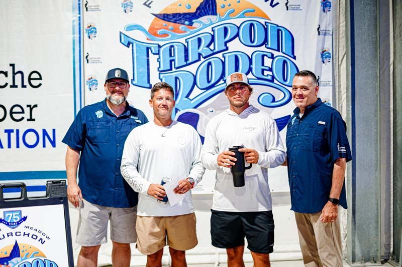 A group of men are standing in front of a tarpon rodeo sign.