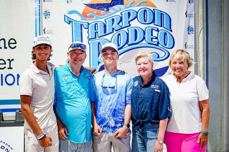 A group of people are posing for a picture in front of a tarpon rodeo sign.