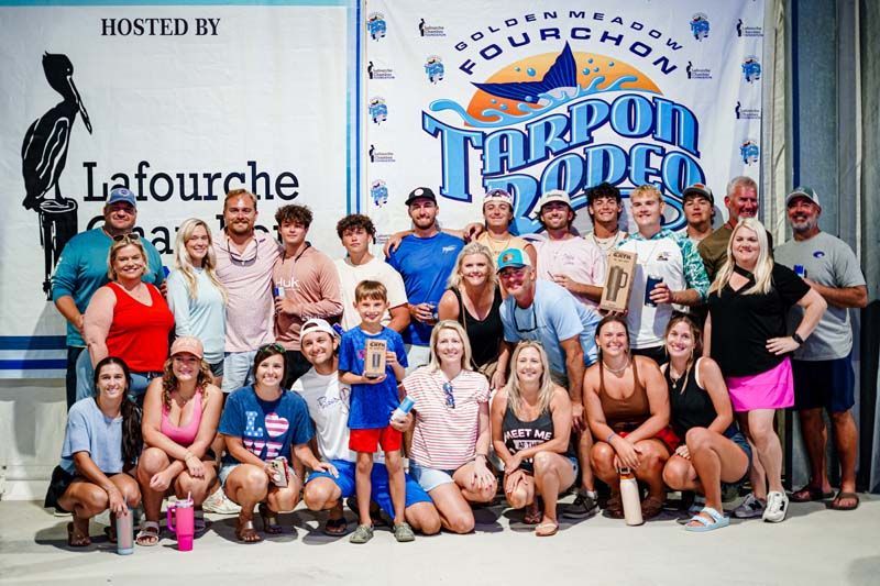 A large group of people are posing for a picture in front of a banner that says tarpon rodeo.