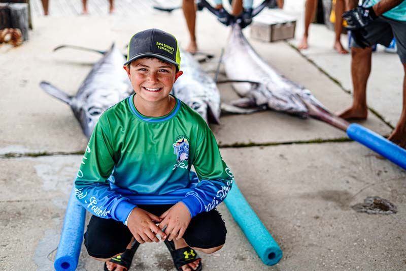 A young boy is kneeling down next to a large fish.