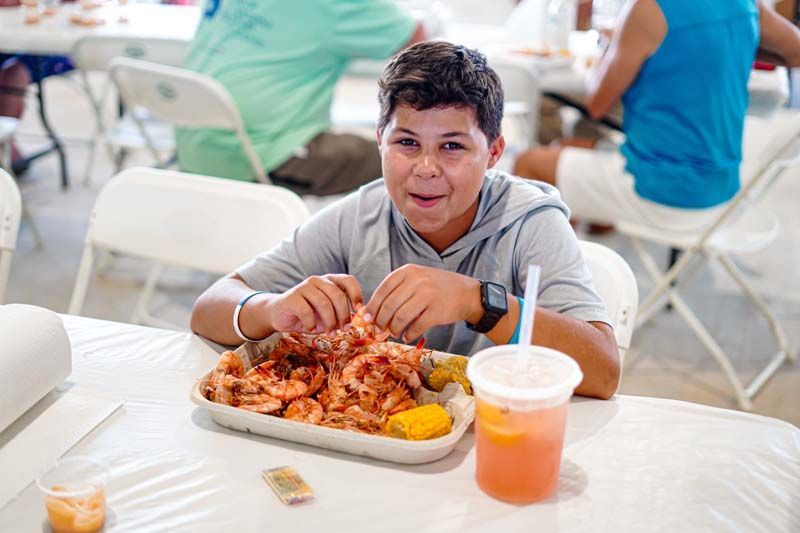 A young boy is sitting at a table eating shrimp.
