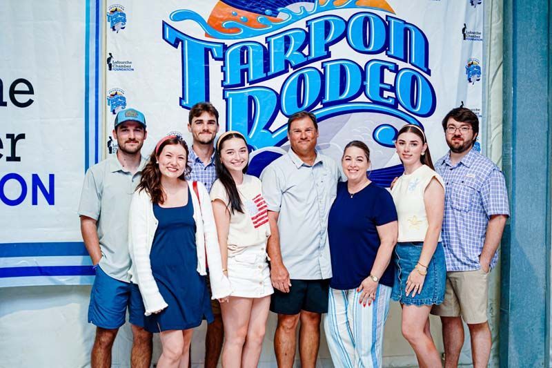 A group of people are posing for a picture in front of a tarpon rodeo sign.