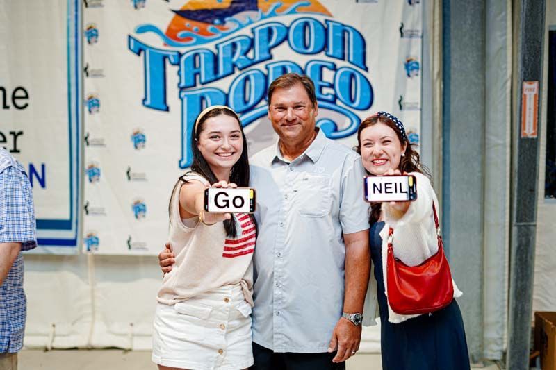 A group of people are posing for a picture in front of a tarpon rodeo sign.