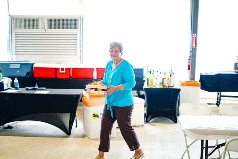A woman is walking through a room holding a tray of food.