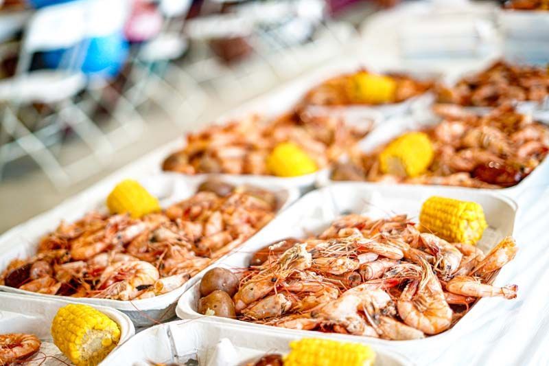 A table topped with trays of shrimp and corn on the cob.
