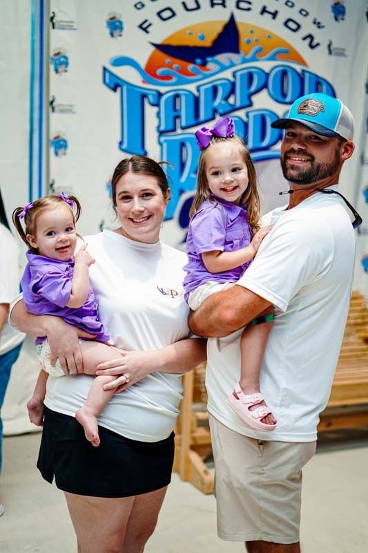 A man and woman are holding two little girls in front of a tarpon park sign.