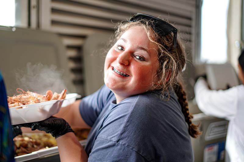 A woman with braces is smiling while holding a tray of shrimp.