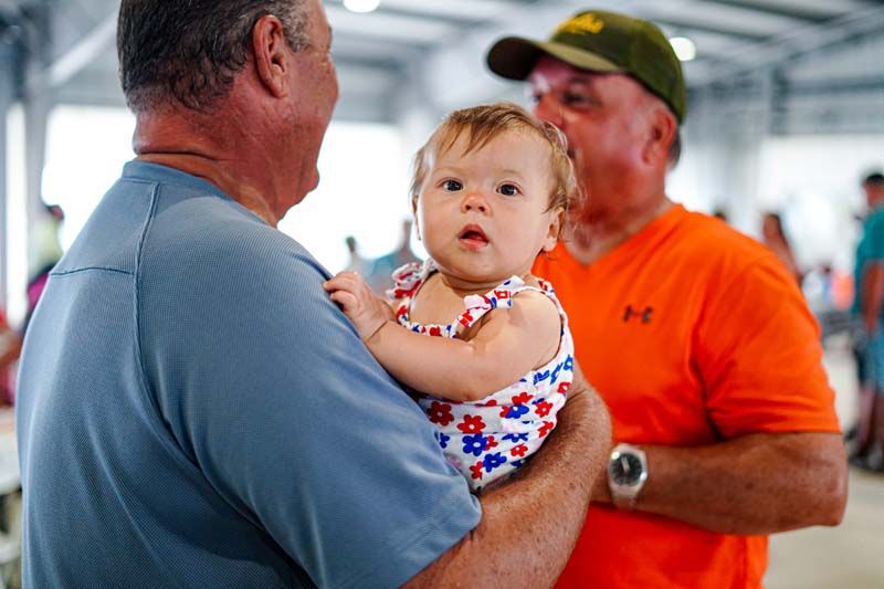 A man is holding a baby in his arms while another man looks on.