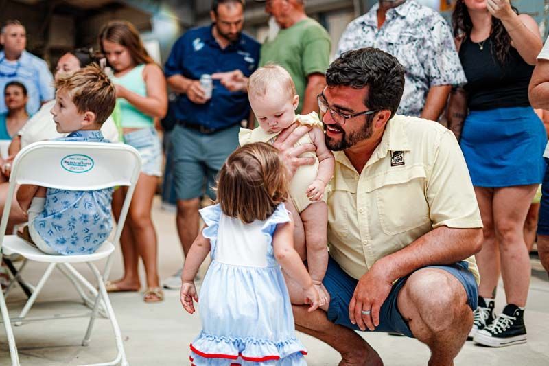 A man is kneeling down holding a baby and a little girl.