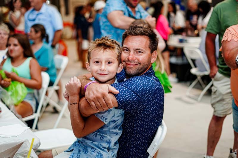 A man is holding a little boy in his arms at a party.