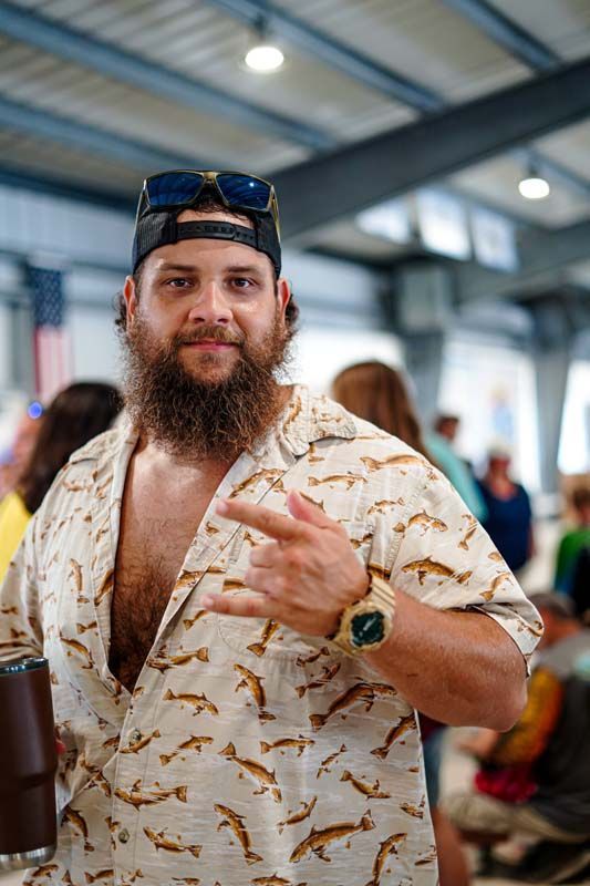 A man with a beard is wearing a hat and sunglasses and holding a beer.