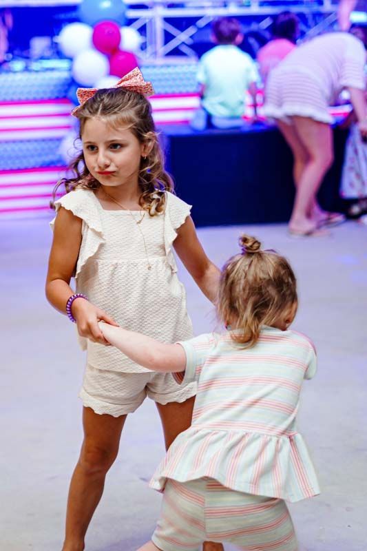 Two little girls are dancing together at a party.
