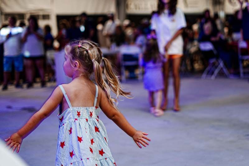A little girl in a dress is dancing in front of a crowd.
