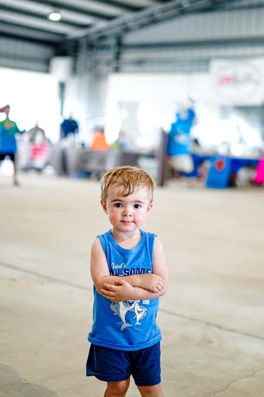 A little boy in a blue tank top and blue shorts is standing with his arms crossed.
