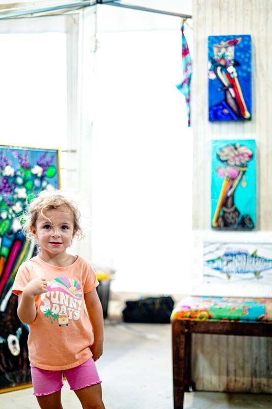 A little girl is standing in a room with paintings on the wall.