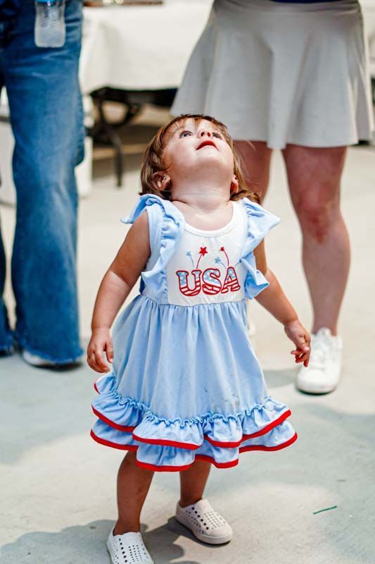 A little girl in a blue and white dress is looking up.