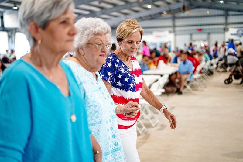 Three older women are standing next to each other in a crowded room.