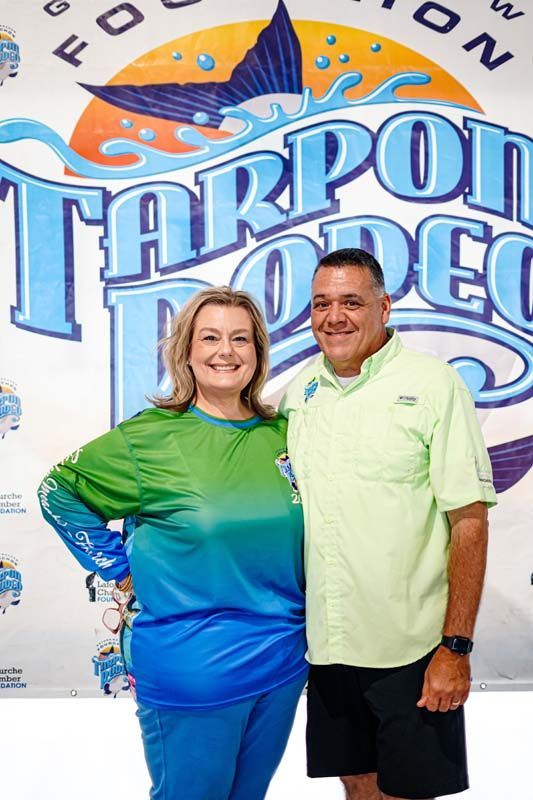 A man and a woman are posing for a picture in front of a tarpon rodeo sign.