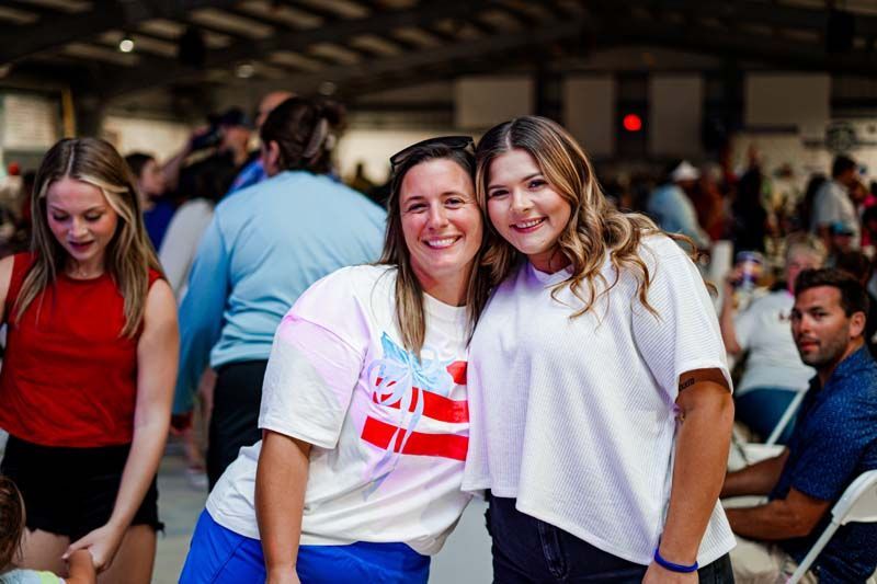 Two women are posing for a picture together in a crowded room.