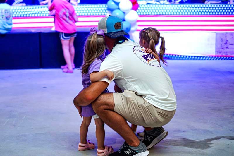 A man is kneeling down with two little girls at a carnival.