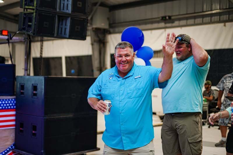 Two men are standing next to each other in a room with balloons and speakers.