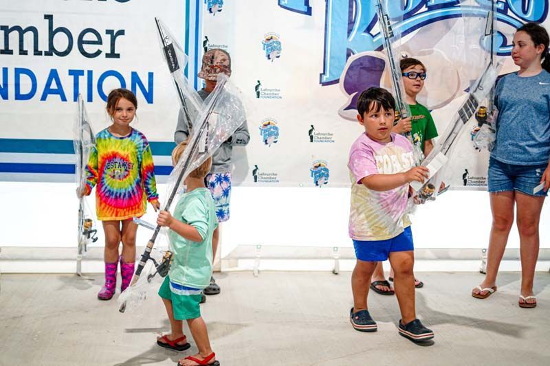 A group of children are holding fishing rods in front of a sign that says mber foundation.