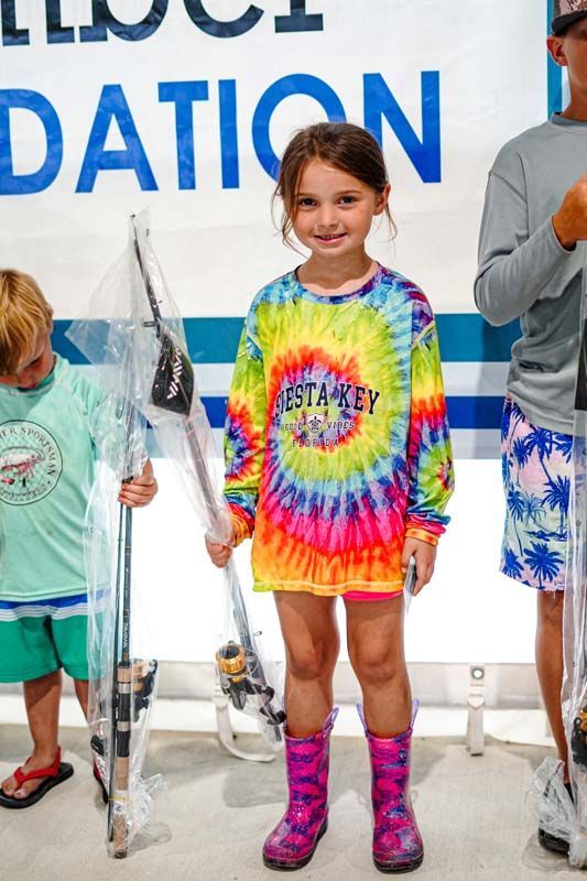A little girl in a tie dye shirt is holding a fishing rod.
