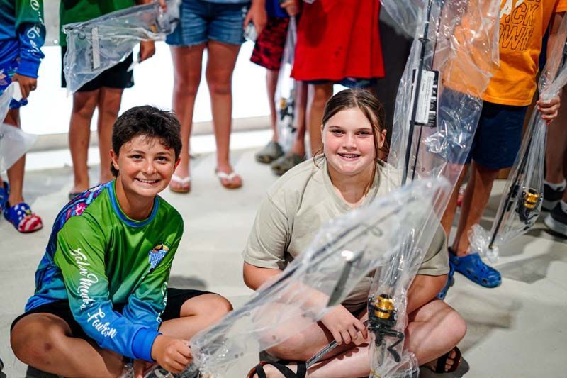 A boy and a girl are sitting on the ground holding fishing rods.