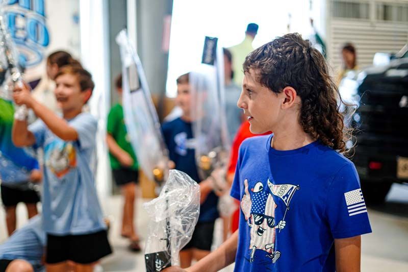 A boy in a blue shirt is standing in front of a group of children holding flags.