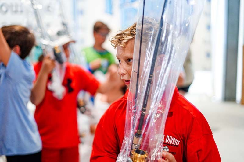 A boy in a red shirt is holding a plastic bag over his head.