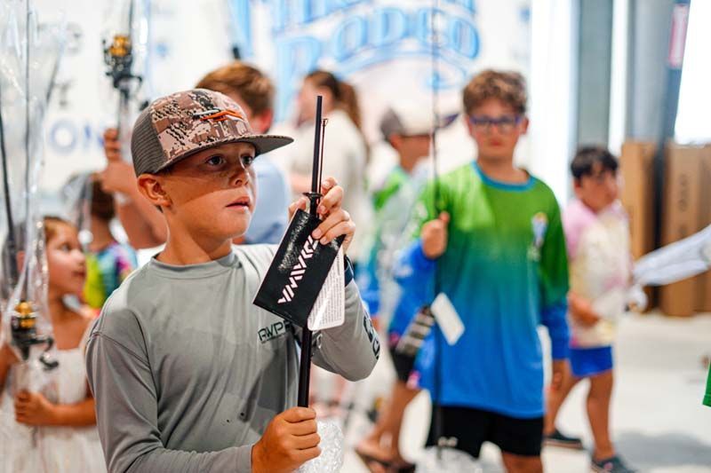 A young boy is holding a fishing rod in front of a group of people.