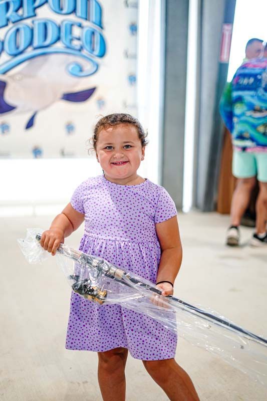 A little girl in a purple dress is holding a fishing rod.