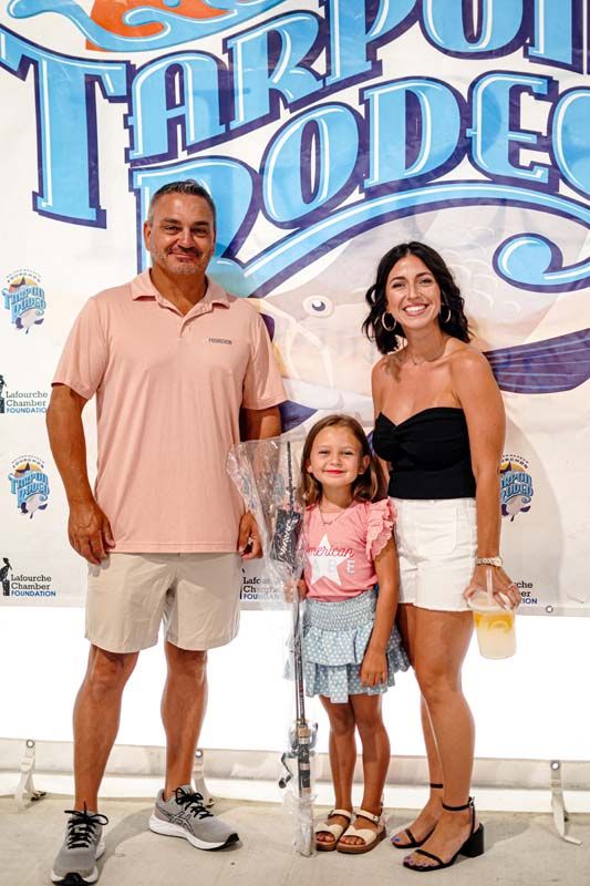 A man , woman and child are posing for a picture in front of a sign.