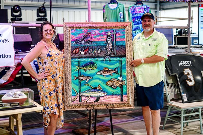 A man and a woman are standing next to each other holding a framed painting of fish.