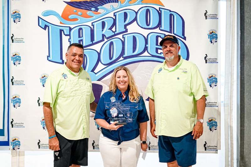 Three people are standing in front of a tarpon dodge sign.