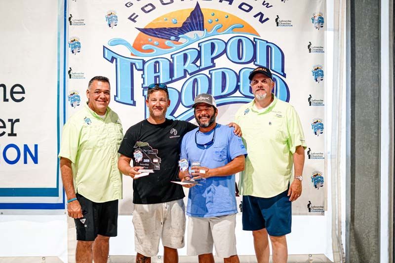 A group of men are posing for a picture in front of a tarpon fishing sign.