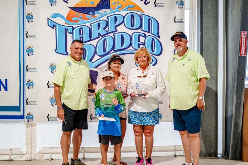 A group of people standing in front of a tarpon rodeo sign.