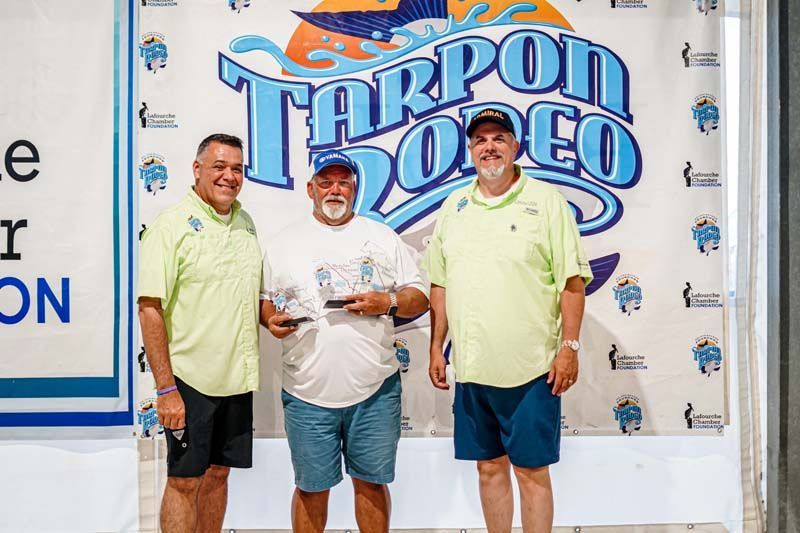 Three men are standing in front of a tarpon doco sign.