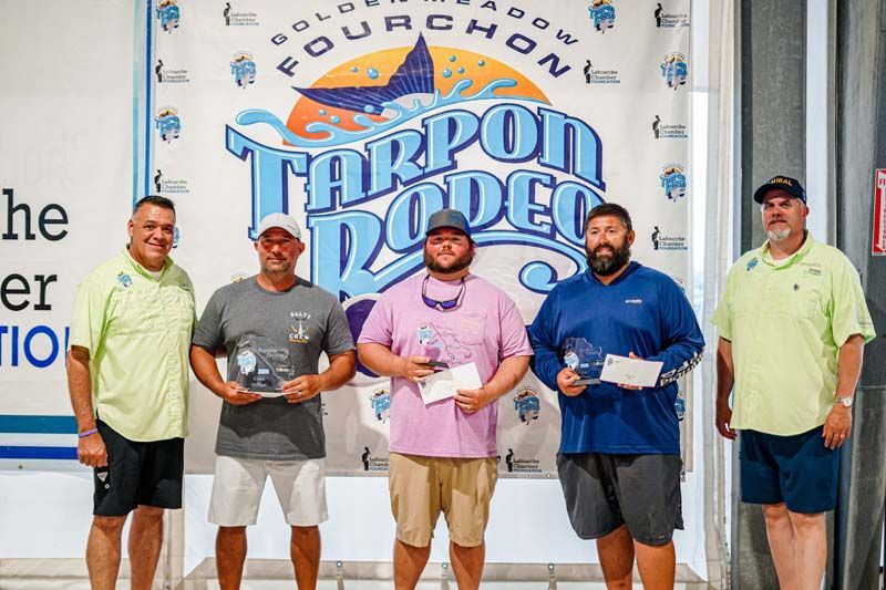 A group of men are standing in front of a sign that says tarpon rodeo.