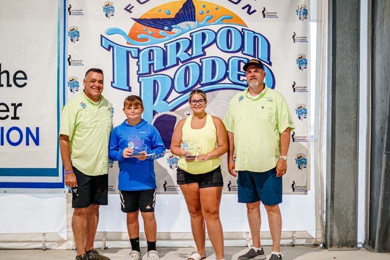 A group of people standing in front of a tarpon rodeo sign.